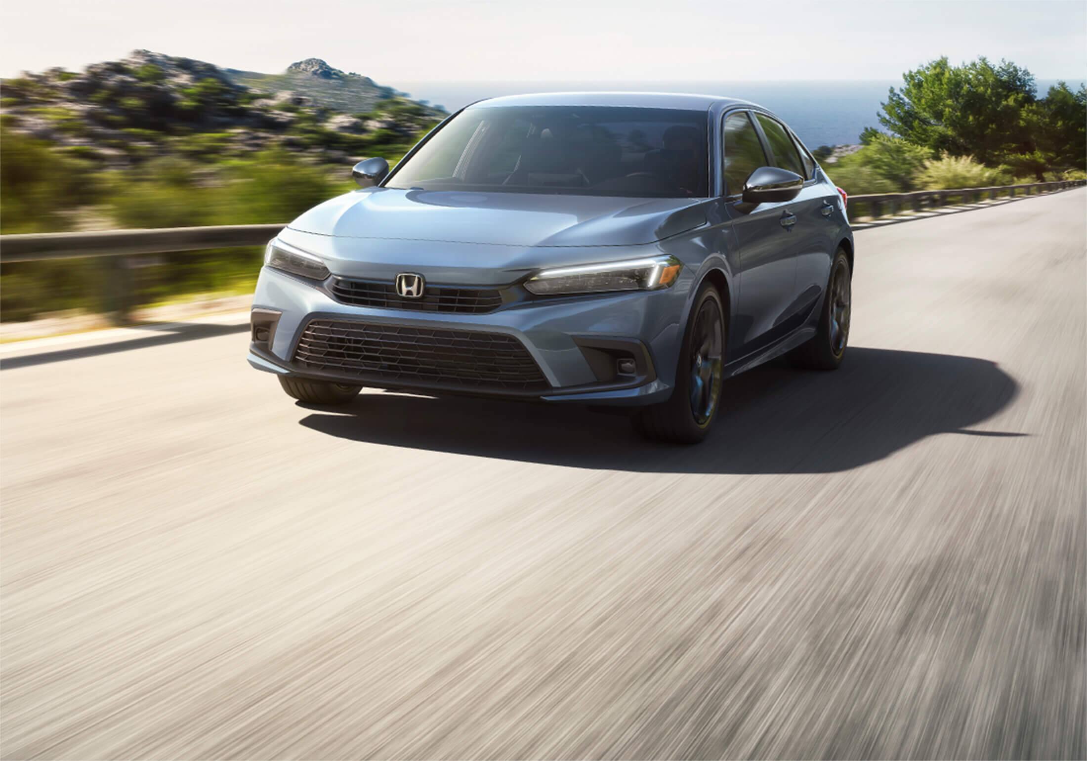 Front driver-side view of the 2023 Honda Civic Sport Sedan in Sonic Gray Pearl, accelerating up a hill.