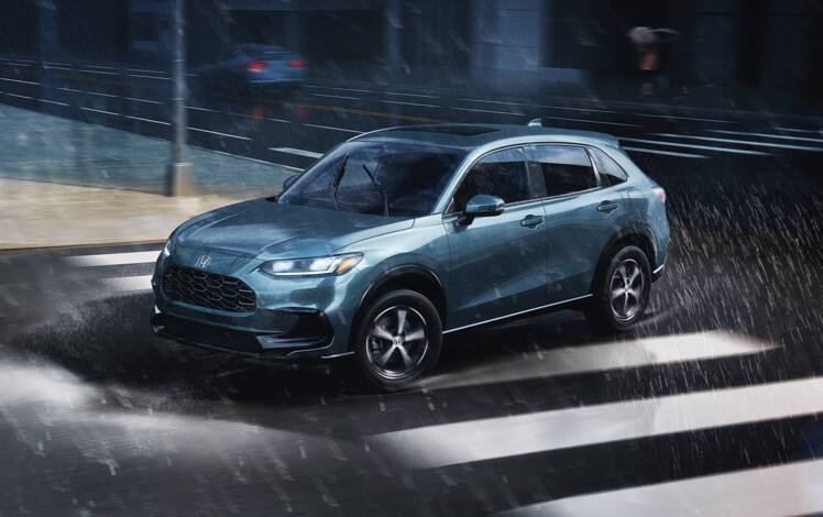 Front driver-side view of the 2023 Honda HR-V EX-L in Nordic Forest Pearl, driving in an urban environment during a rainstorm.