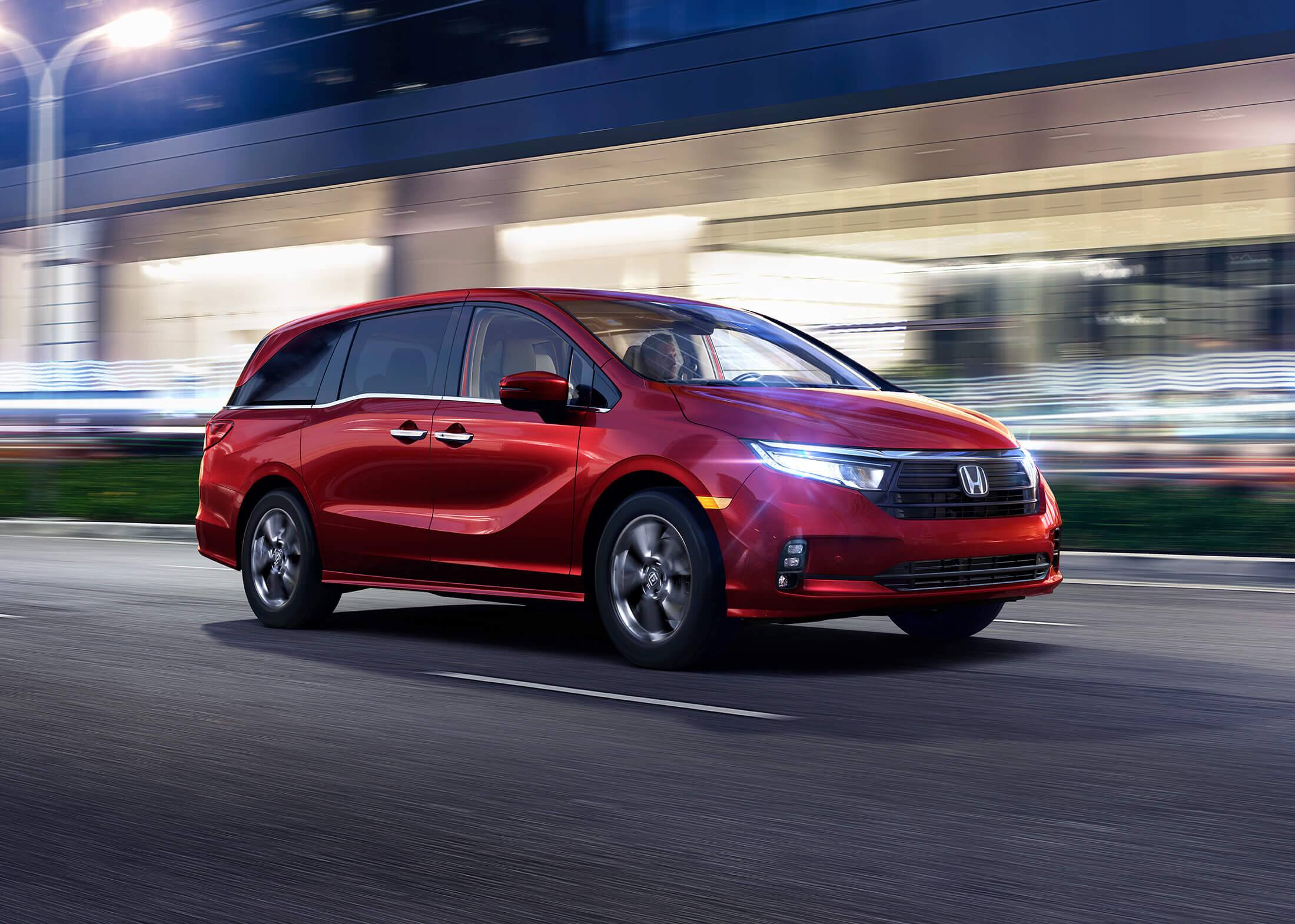 Front passenger-side view of the 2023 Honda Odyssey Elite in Radiant Red Metallic II driving on a city street.